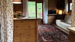 Interior acolhedor de cabana com teto de madeira, sofá, televisão, tapete estampado e janela com cortinas.