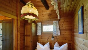 Quarto de cabana de madeira com cama, luminária pendente, janela com cortinas e porta.