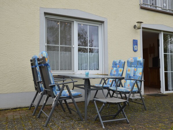 A patio with a table and four chairs, a window, and a door leading to a room. - Comfy Apartment in Gransdorf With Garden (Gransdorf)