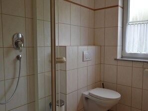 Un baño con ducha, inodoro y ventana con cortinas.