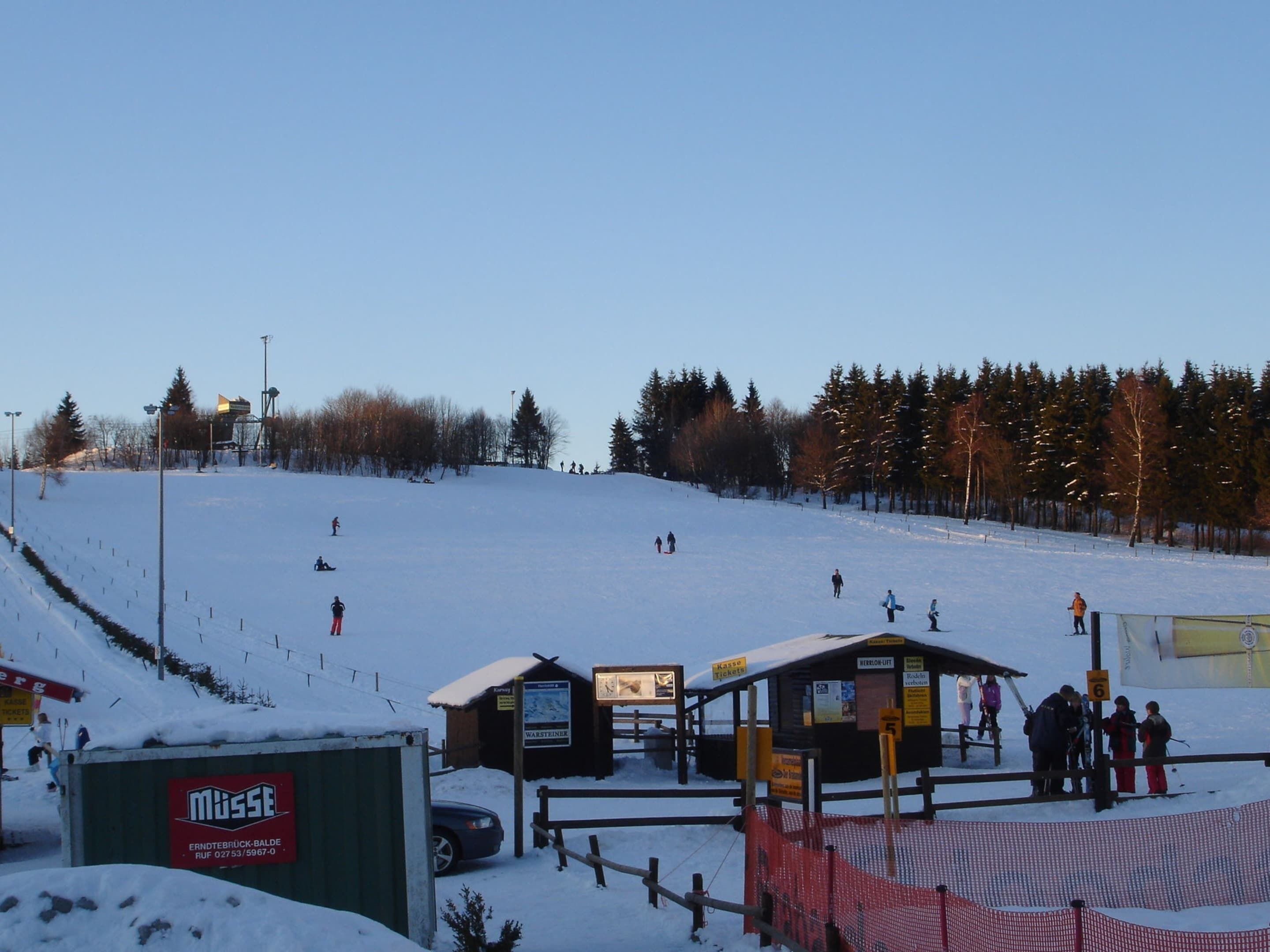 Een skigebied met een skilift, een loket en een klein gebouwtje met een bord.