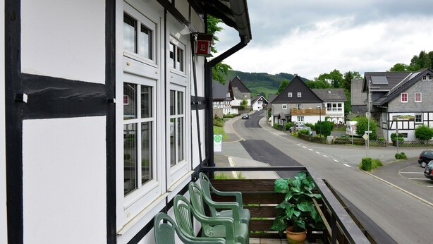Un edificio tradizionale con struttura a telaio a vista, un balcone, e un'auto parcheggiata di fronte.