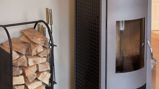 A modern wood-burning stove with a glass door, a metal rack for logs, and brass candle holders. - Ferienhaus in Rechenberg-bienemuehle (Rechenberg-Bienenmuehle)