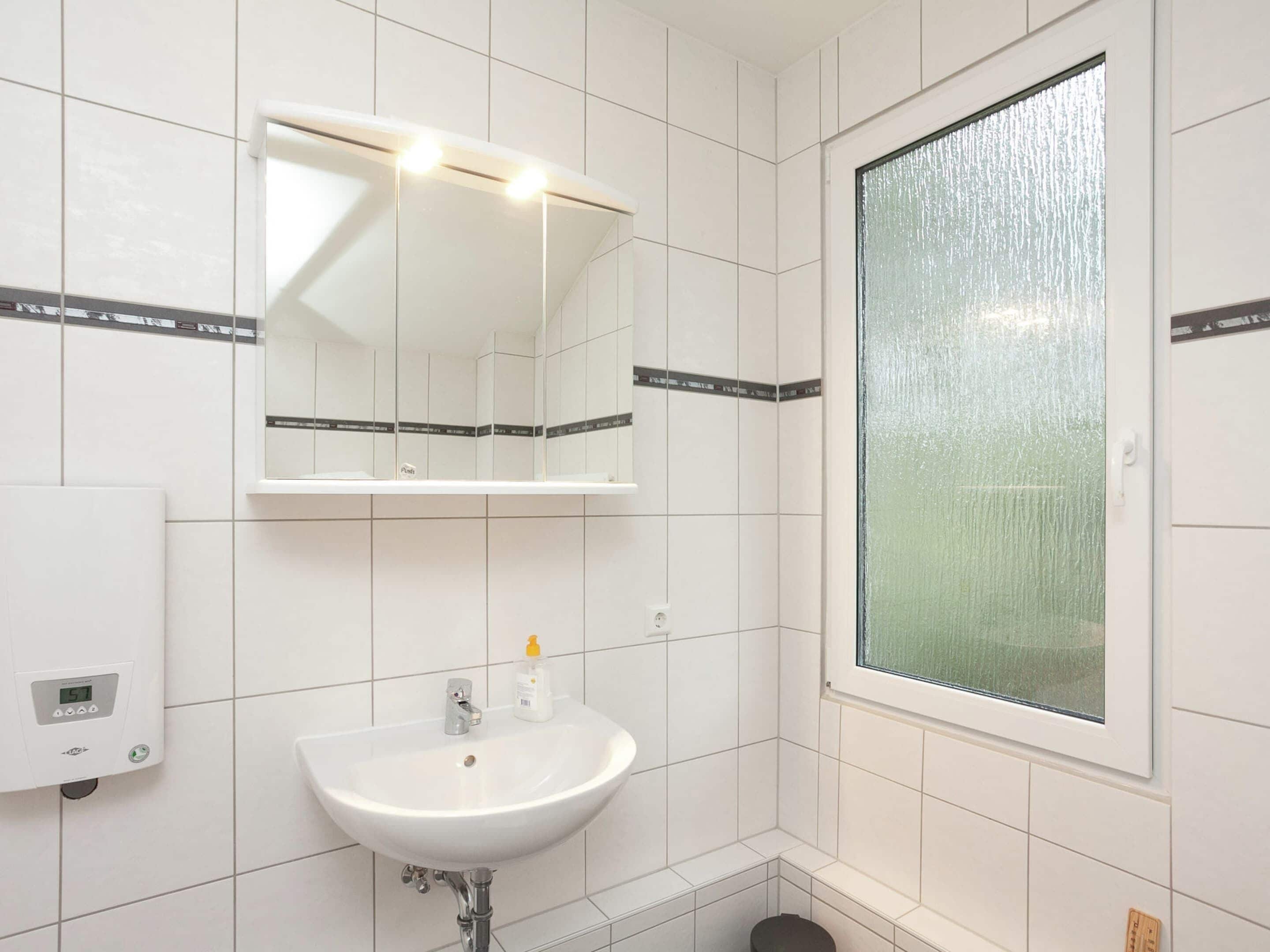 A bathroom with a white sink, a mirror, and a window with a frosted glass.