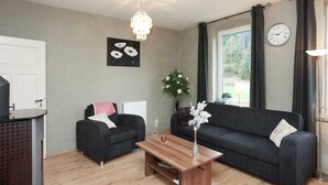 A modern living room with two dark sofas, a wooden coffee table, a chandelier, a clock, and a window with curtains. - Ferienhaus in Rechenberg-bienemuehle (Rechenberg-Bienenmuehle)