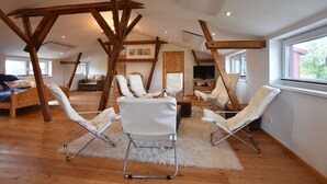 A spacious loft with wooden beams, white leather chairs, a wooden bed, and a large window offering a view. - Exquisite Mansion in Pugholz near Sea (Hasselberg)