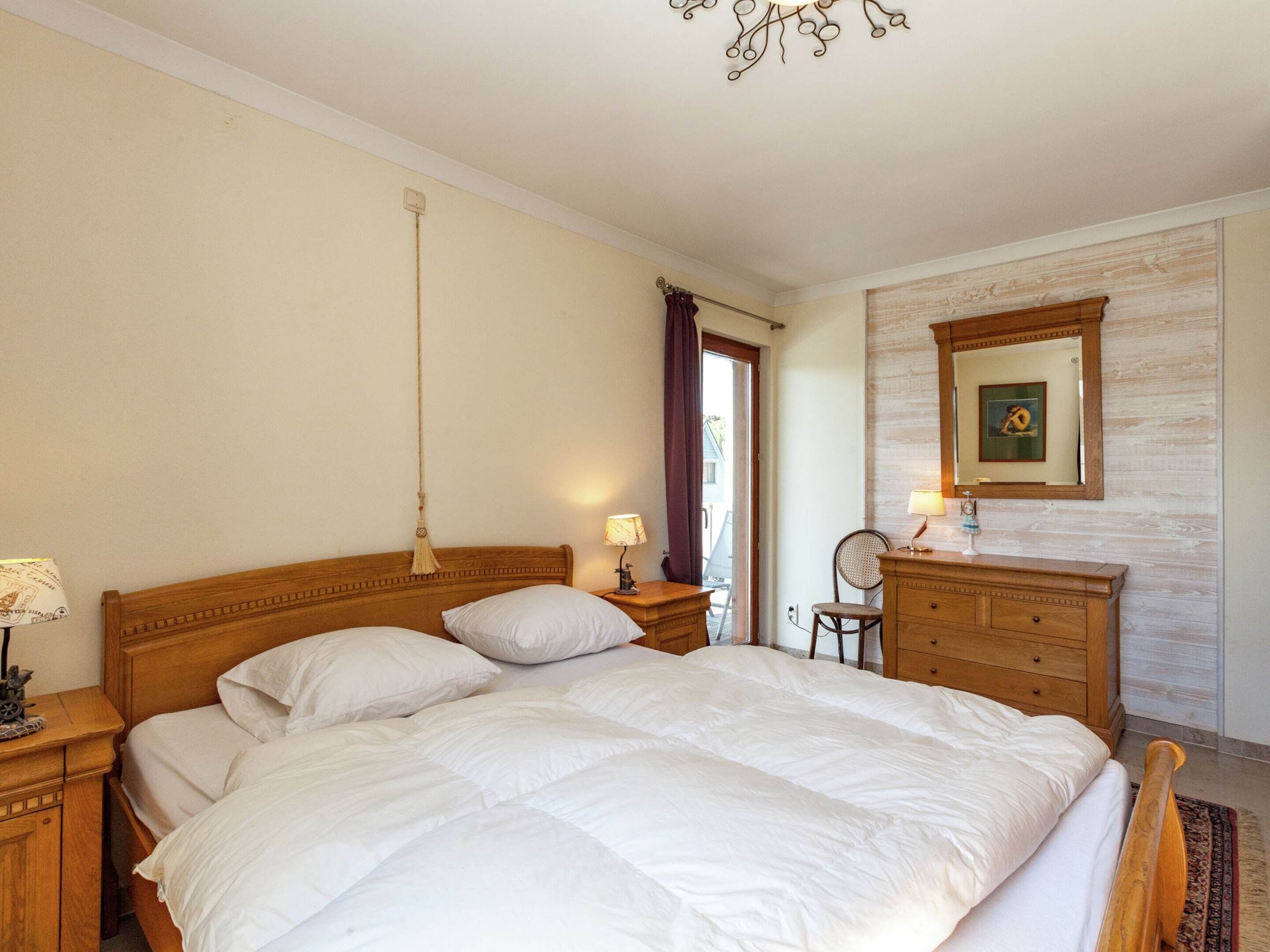 A bedroom with a large bed, wooden headboard, bedside tables with lamps, a dresser, and a mirror on the wall.