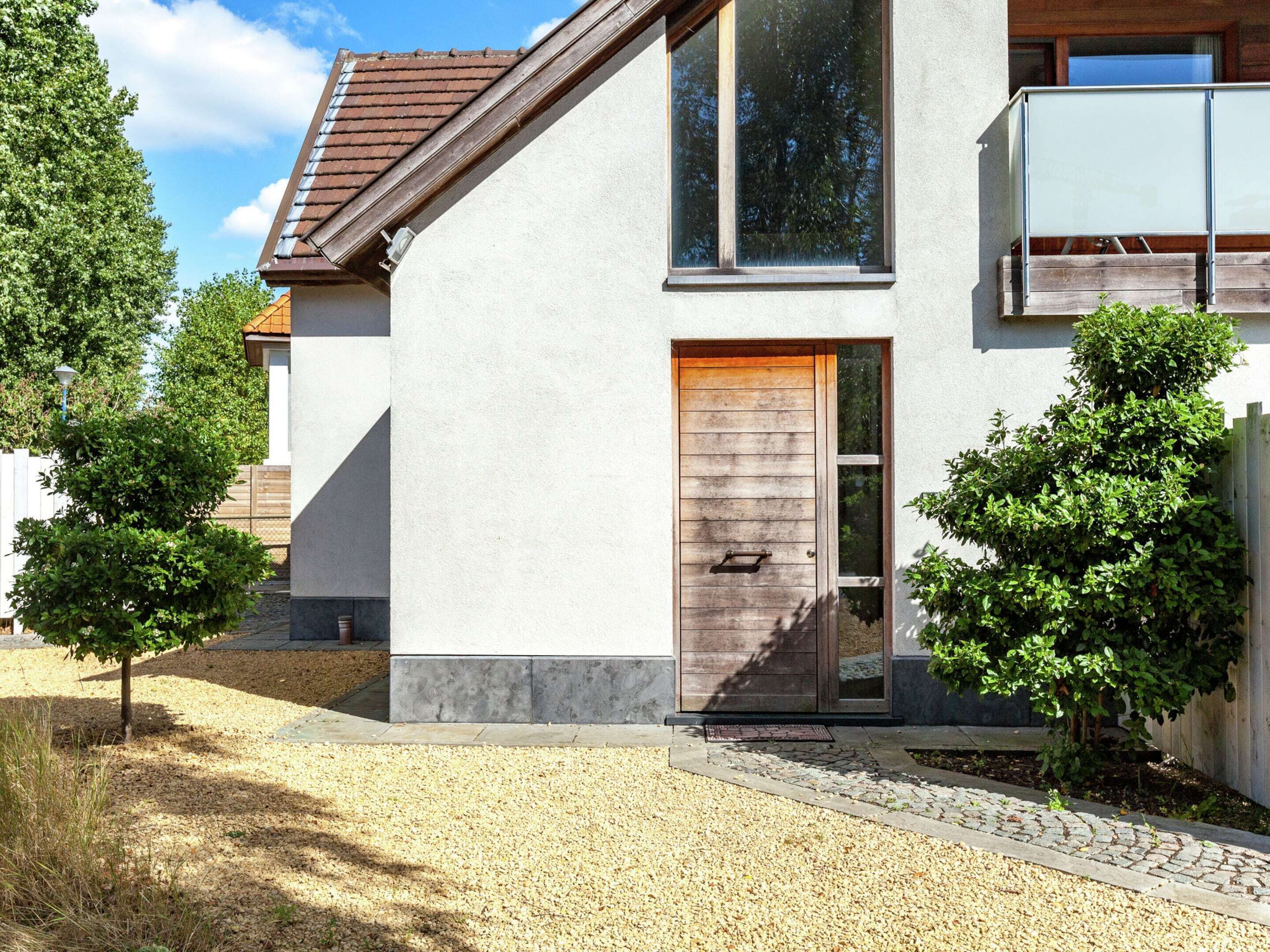 Een modern huis met een groot raam, een houten deur en een kleine boom in de voortuin.