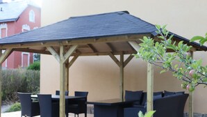 An outdoor patio with a wooden pergola, black furniture, and a small tree with green leaves. - Heritage Villa With Home Cinema, Sauna (Treuen)