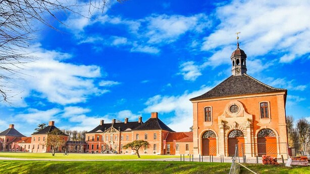 A historic building with a prominent clock tower, surrounded by well-maintained lawns and a small water feature. - Ferienhaus in Thorstorf mit Garten (Warnow)