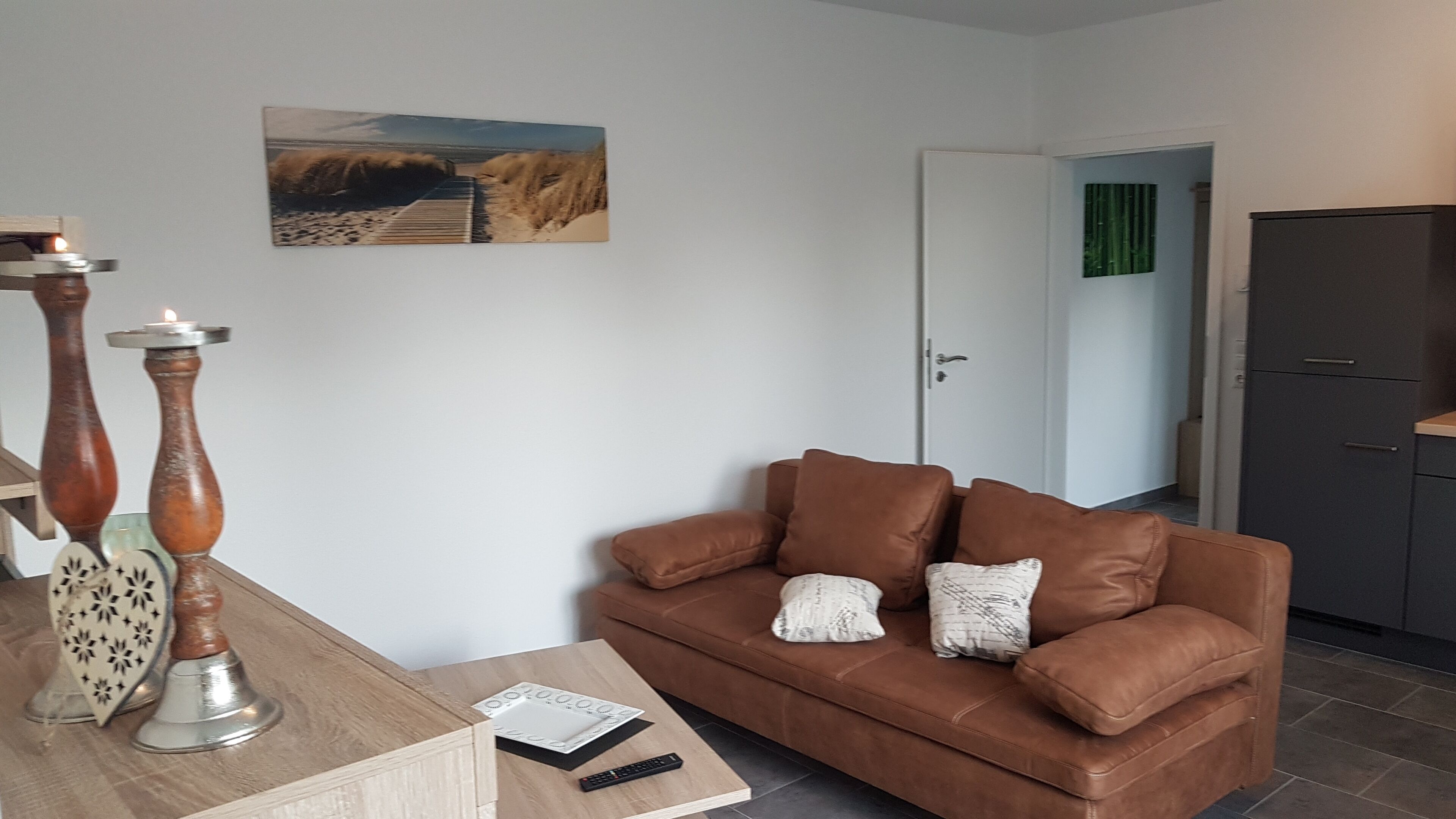 Een woonkamer met een bruine leren bank, een houten salontafel, twee decoratieve vazen en een schilderij van een strand.