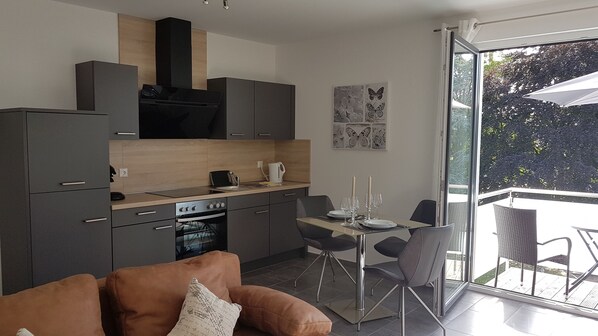 A modern kitchen with dark cabinetry, a built-in oven, and a dining area with a table and chairs.