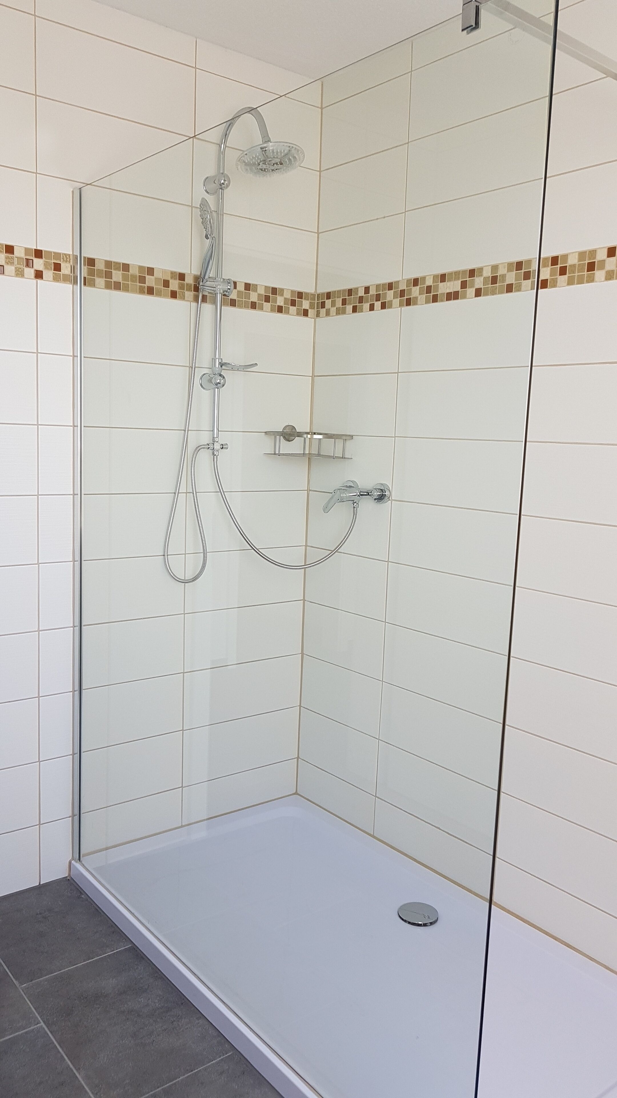 Una cabina de ducha con paredes de vidrio, suelo de baldosas y ducha en esquina.