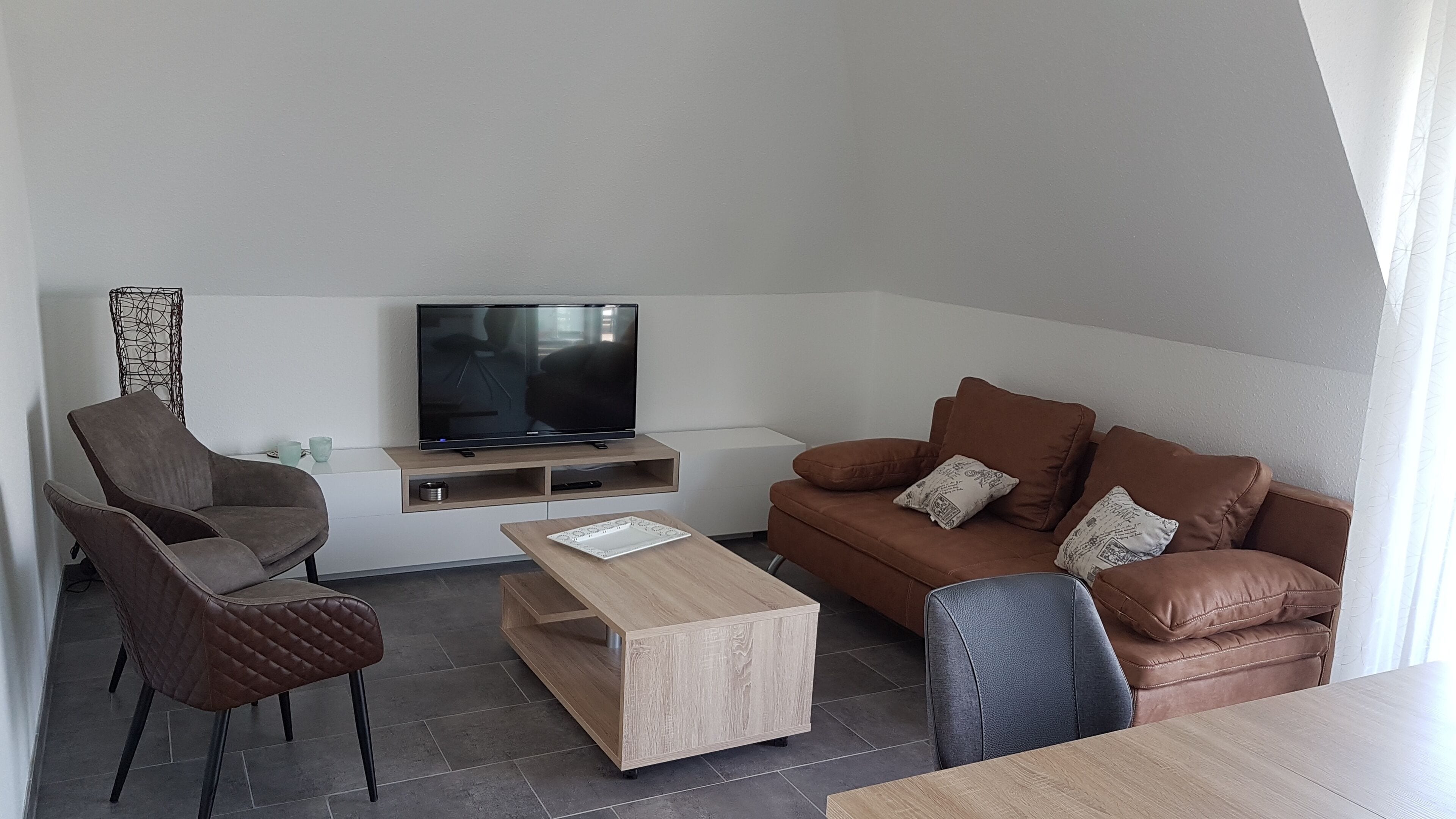 Una sala de estar moderna con sofá, mesa de centro, televisor y una silla.
