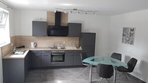 A modern kitchen with grey cabinetry, a built-in oven, and a glass dining table with black chairs.