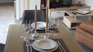 En matplats med ett bord dukat för fyra personer, en tv i bakgrunden och ett träskåp ovanför bordet.