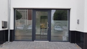 En byggnadsentré med en glasdörr som speglar parkerade bilar och en person som står inne i byggnaden.