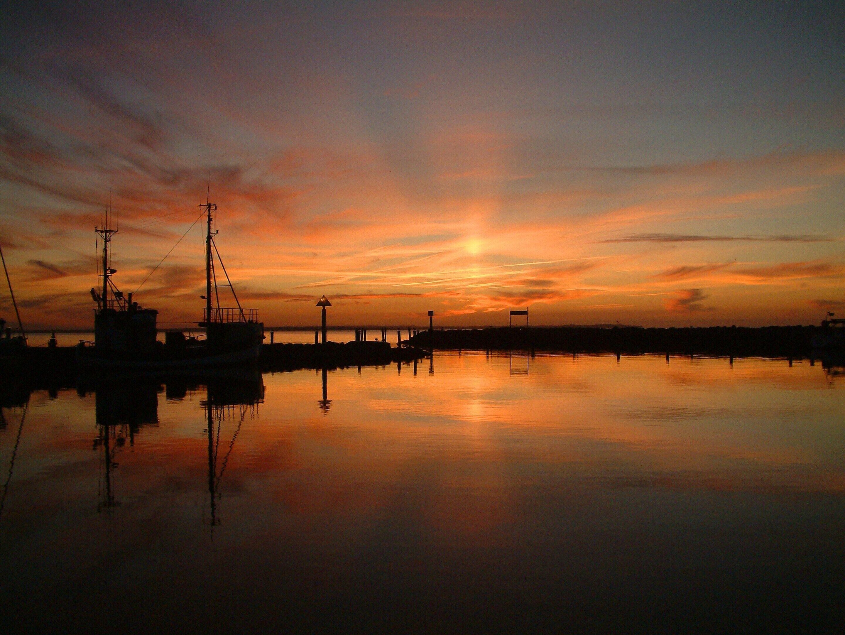 A calm harbor at sunset with boats and a pier.
