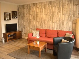 Ein Wohnzimmer mit Holzpaneelen, einem roten Sofa, einem schwarzen Sessel, einem Holztisch und einer TV-Konsole.