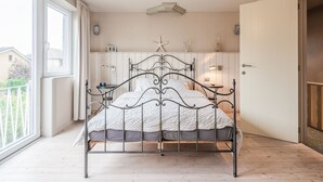 Une chambre à coucher avec un lit en métal, une table de chevet, une lampe et une fenêtre avec des rideaux.