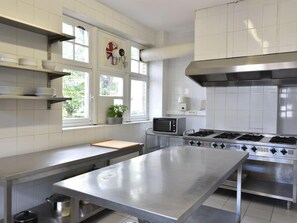 Enjoy cooking in this well-equipped kitchen with a large stainless steel table, microwave, gas stove, and ventilation hood.