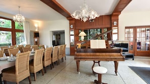 A dining area with a piano, wicker chairs, and a chandelier. - Former Hotel in the Centre and Near the Beach in Panne (De Panne)