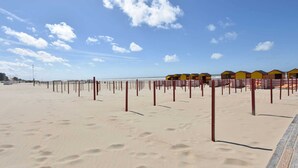 A beach with rows of yellow beach huts and red poles. - Former Hotel in the Centre and Near the Beach in Panne (De Panne)
