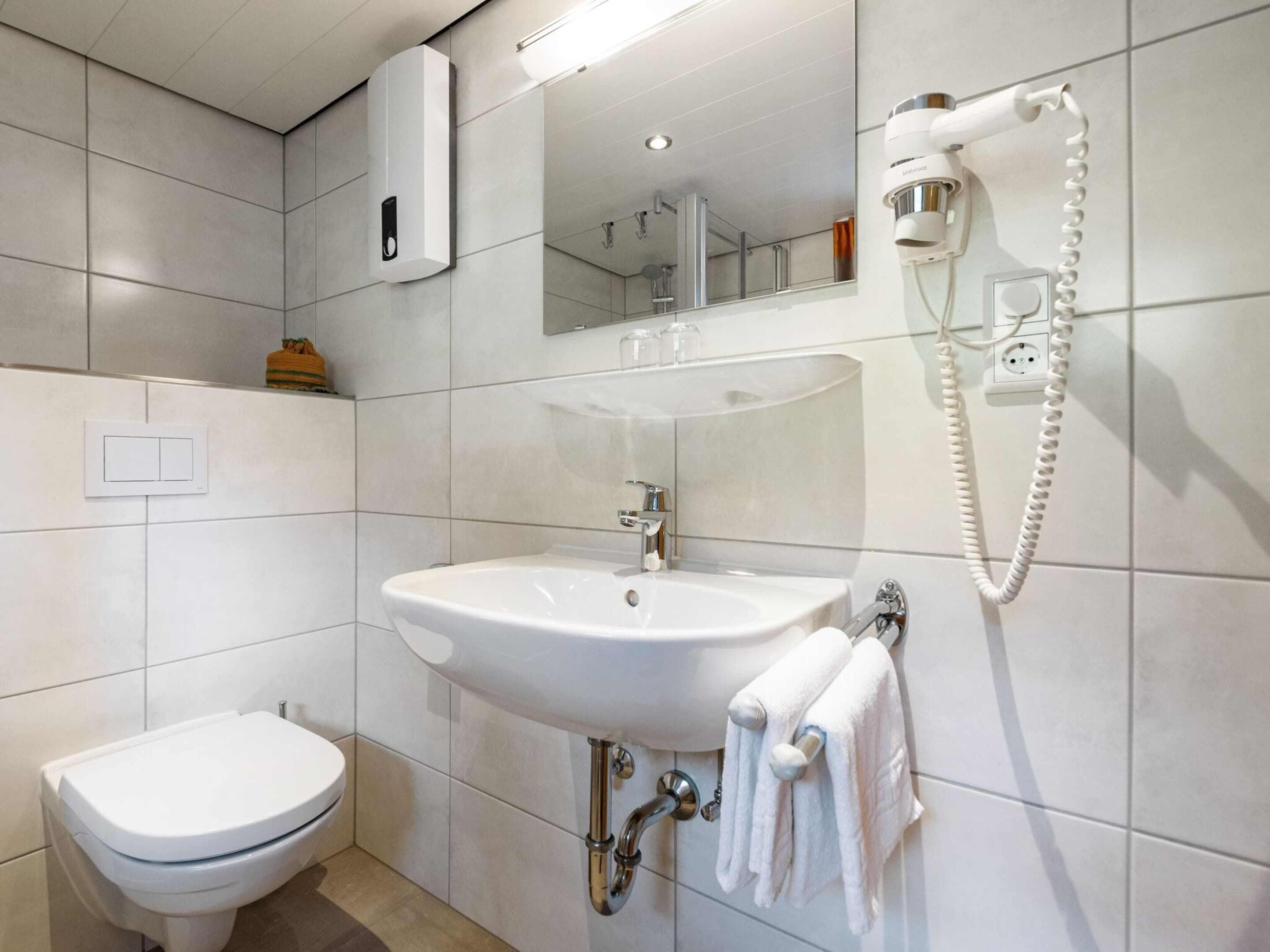 Un bagno moderno con lavandino, water e asciugacapelli montato a parete.