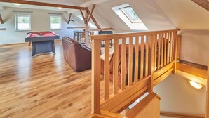 Un loft amplio con pisos de madera, una mesa de futbolín, un sofá y una escalera con barandilla de madera.