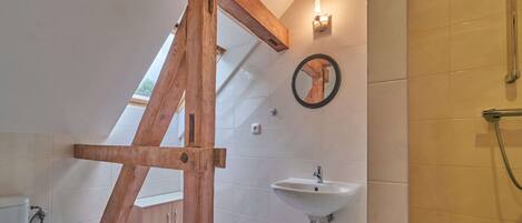 Un baño con estructura de vigas de madera, un lavabo, un espejo y una ducha.