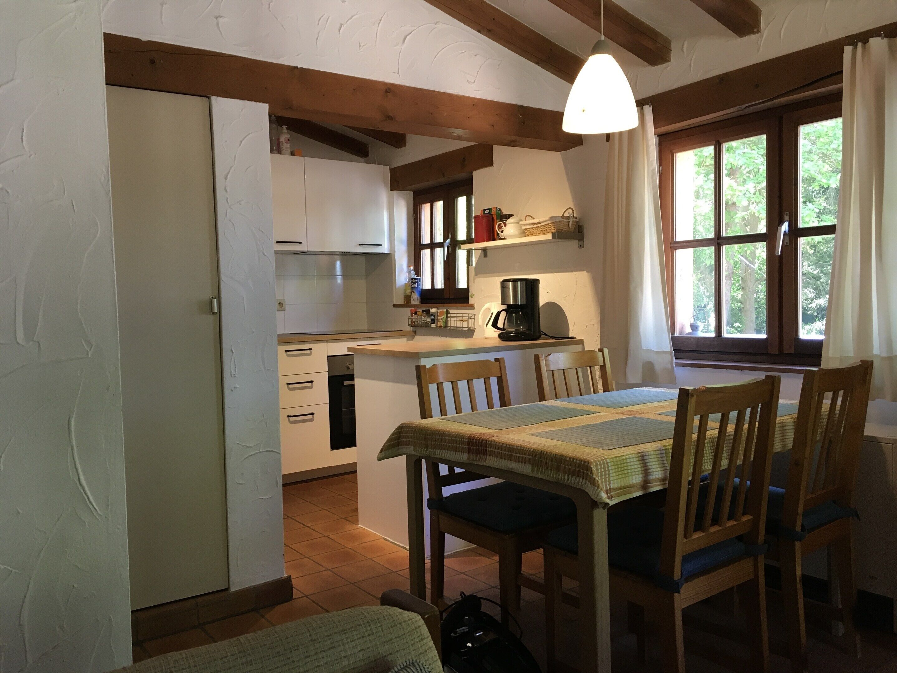 A cozy kitchen with wooden beams, a dining table with chairs, and a window with curtains.
