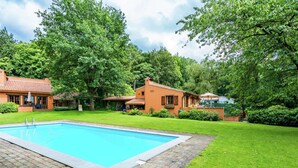 A swimming pool with a paved deck, surrounded by well-maintained grass and trees. - Cosy and Snug Holiday Home With Joint Swimming Pool (Tessenderlo)
