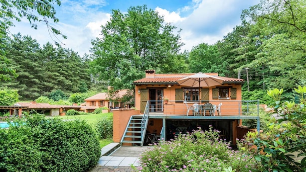 A two-story building with a balcony, surrounded by lush greenery and a swimming pool. - Cosy and Snug Holiday Home With Joint Swimming Pool (Tessenderlo)