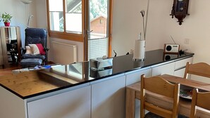 Une cuisine compacte avec un plan de travail noir, des placards blancs, une table à manger en bois et une chaise.