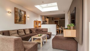 A modern living room with a sectional sofa, a coffee table, and a dining area in the background. - Holiday Home in Kortrijk for 8 Person (Kortrijk)