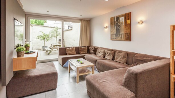 A modern living room with a sectional sofa, a coffee table, and a side table with plants. - Holiday Home in Kortrijk for 8 Person (Kortrijk)