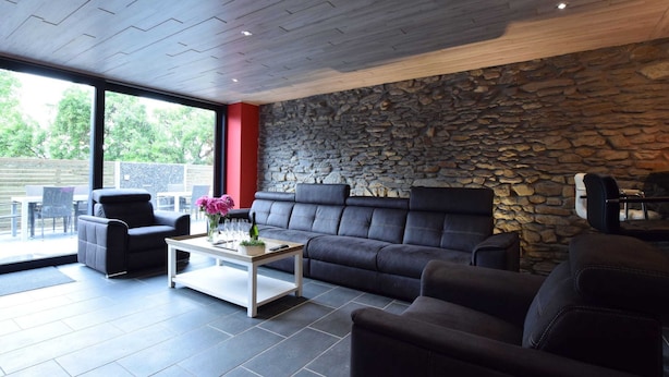 Una sala de estar moderna con una pared de piedra, sofás de cuero y un ventanal con vistas a un jardín.