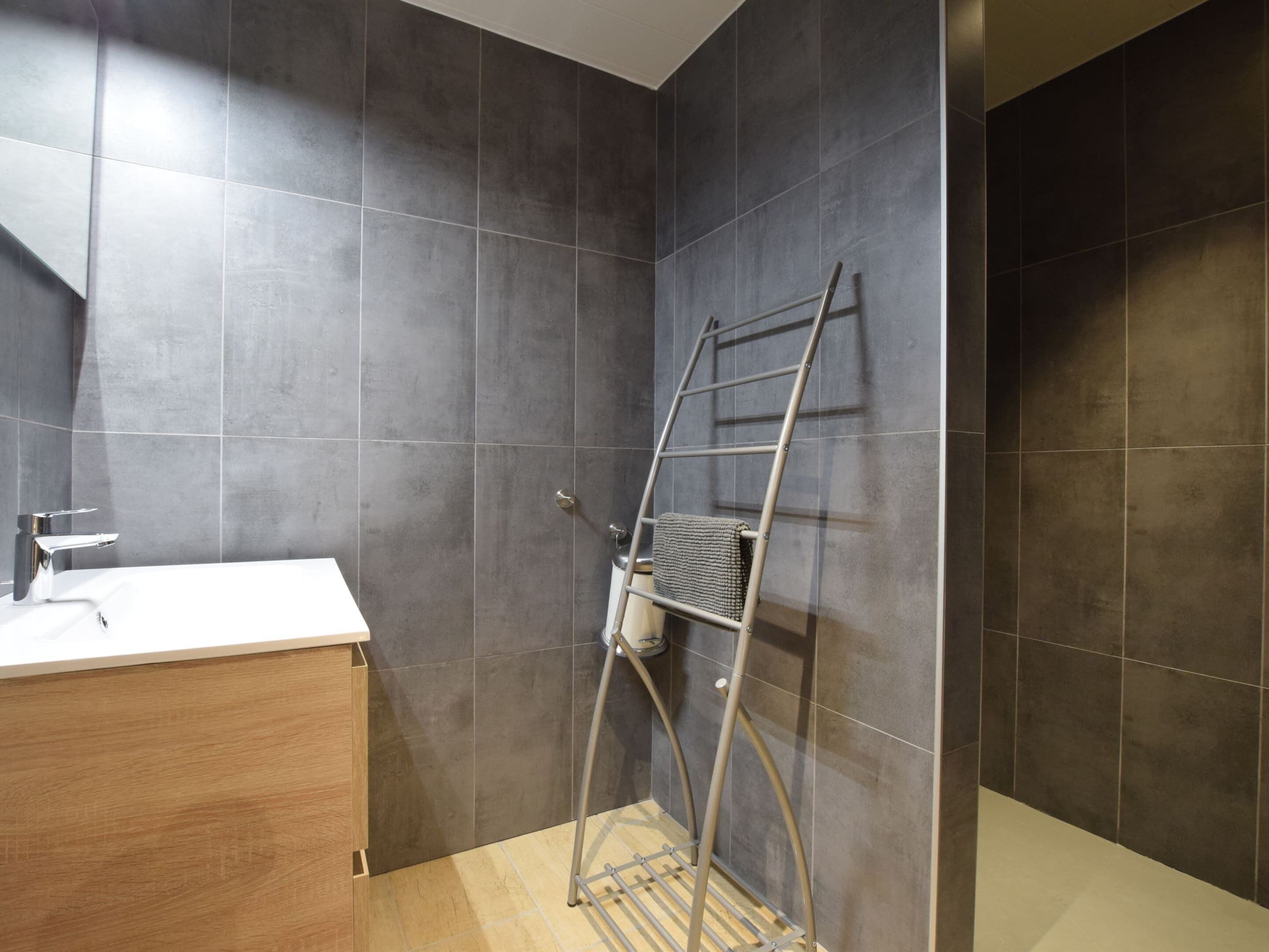 Un baño con paredes de azulejos oscuros, un tocador de madera y un perchero de metal.