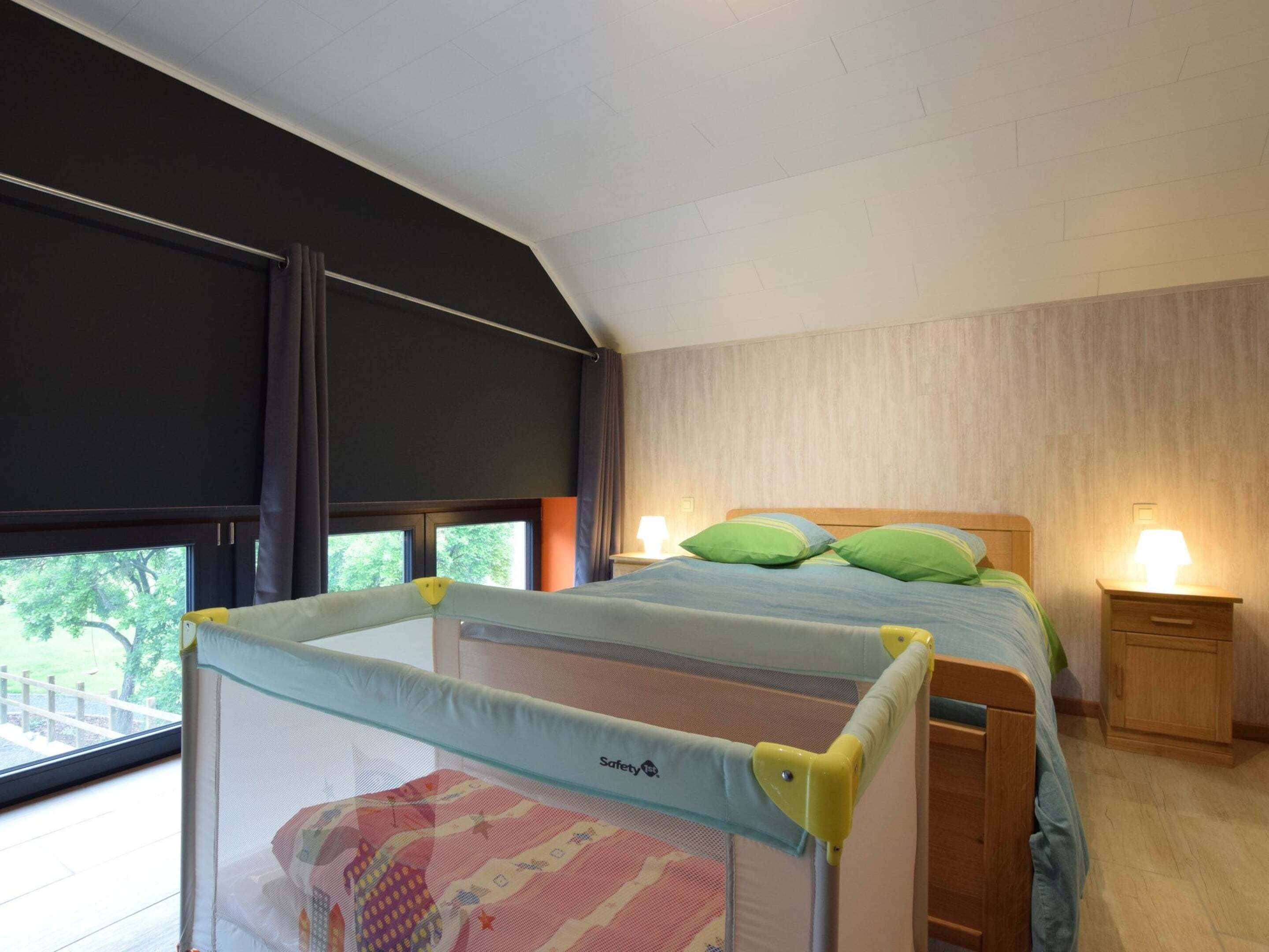 A bedroom with two beds, a window with a view of greenery, and a safety rail around the window.