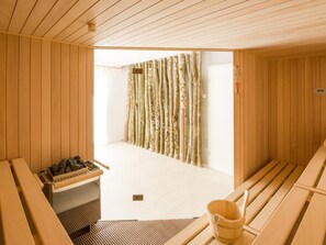 A sauna room with wooden benches, a wooden bench with a bucket, and a sauna bench with a tray of stones. - Apartment in the Black Forest With Balcony (Dachsberg)