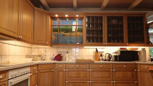 A kitchen with wooden cabinets, a tiled backsplash, and a window with a view of a green landscape. - Alt Krassow Lakeside Retreat (Lalendorf)