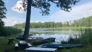 A lakeside picnic area with wooden benches and tables, surrounded by boats and a tree. - Alt Krassow Lakeside Retreat (Lalendorf)