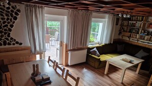 A cozy living room with a wooden dining table, a sofa, and a bookshelf. - House in Bohemian Near Ski Slope (Blatno)
