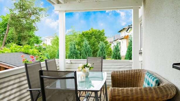 A covered outdoor patio with a table and chairs, surrounded by greenery and buildings in the background. - Apartment in Medebach Near Orketal Reserve (Medebach)