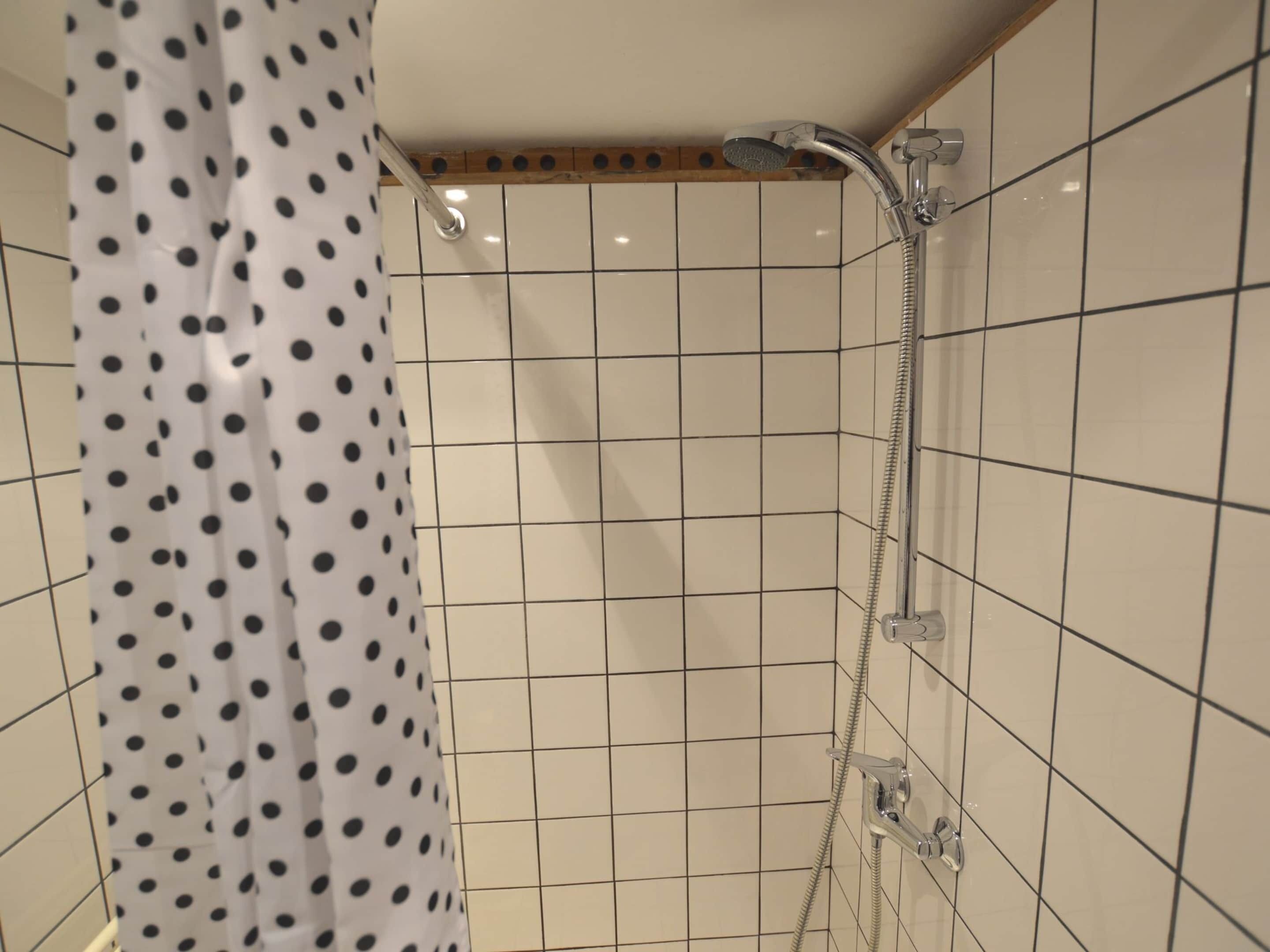 A shower area with a polka dot shower curtain, tiled walls, and a handheld showerhead.