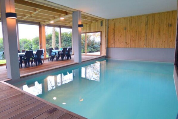 An indoor swimming pool with wooden deck seating and large windows.