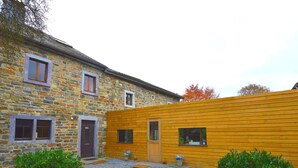 A stone building with a wooden extension, gravel driveway, and green shrubs. - Rustic Farmhouse With Pool (Waimes)