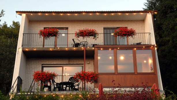 Une maison à deux étages dotée d’un balcon, d’un espace salon extérieur et de guirlandes lumineuses.