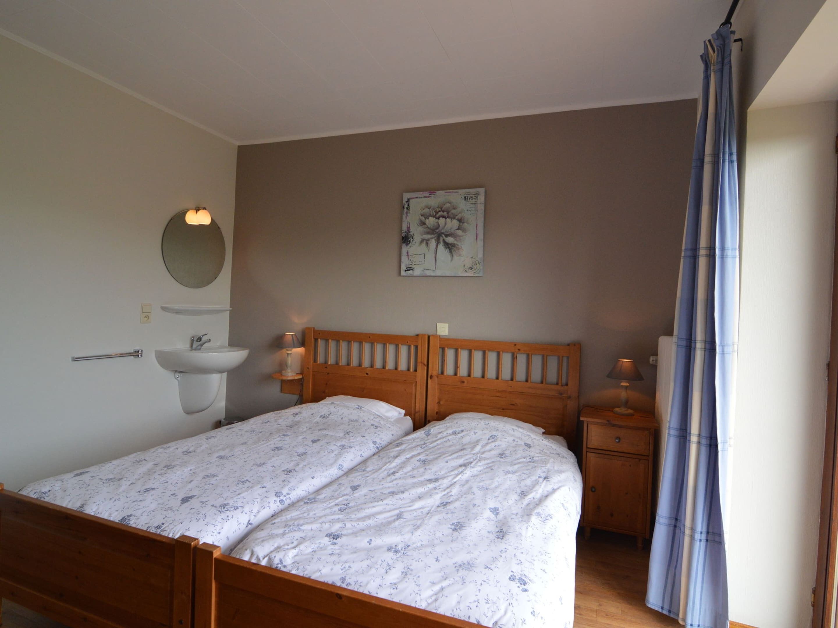 A bedroom with a wooden bed, a bedside table, a nightstand, a wall-mounted sink, and a mirror.