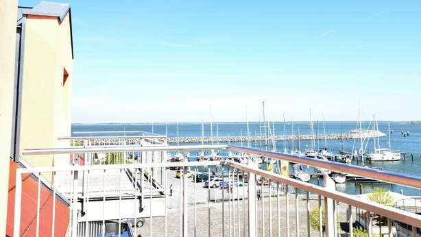 En småbåtshamn med förtöjda båtar, en klar himmel och en byggnad med en balkong som vetter mot vattnet.